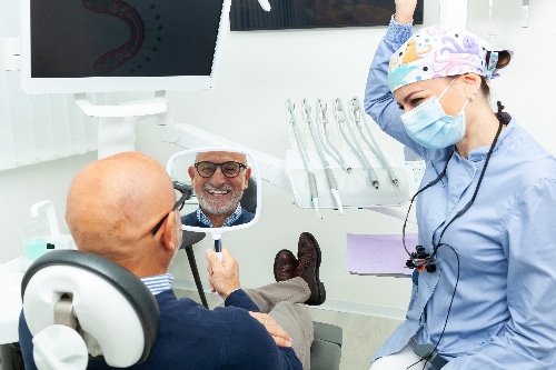 older man smiling in a mirror, happy with new dental implants