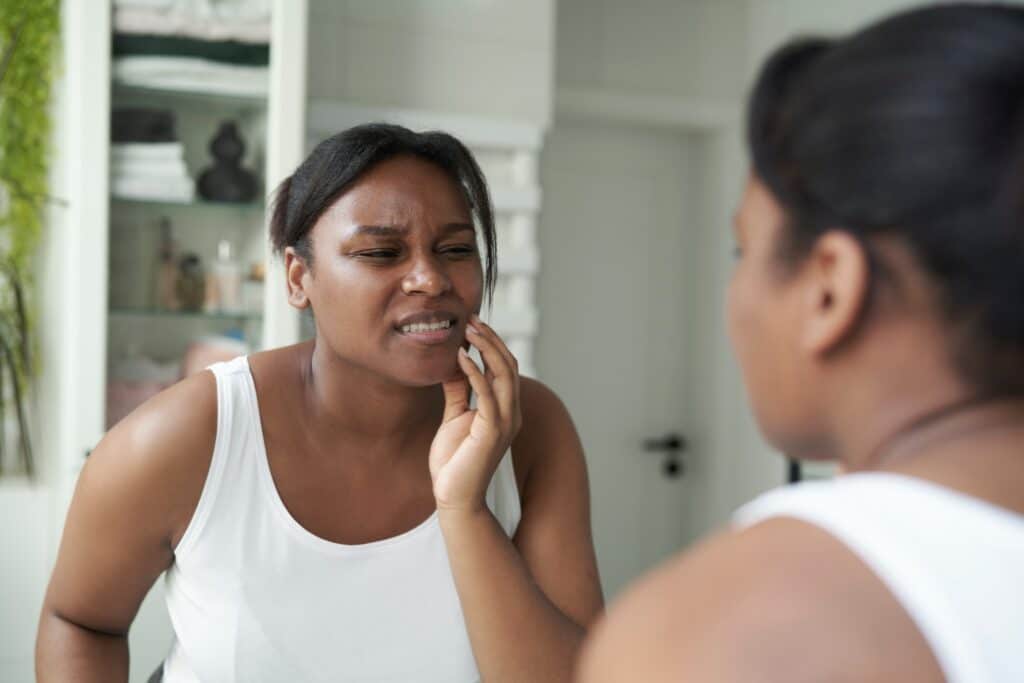 young woman holding her jaw in mirror, pain from bruxism