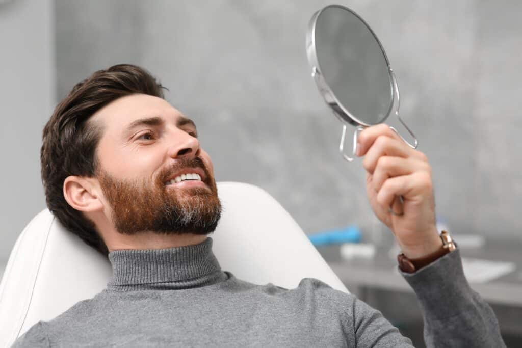 Man looking at his new dental implants in mirror inside dental office